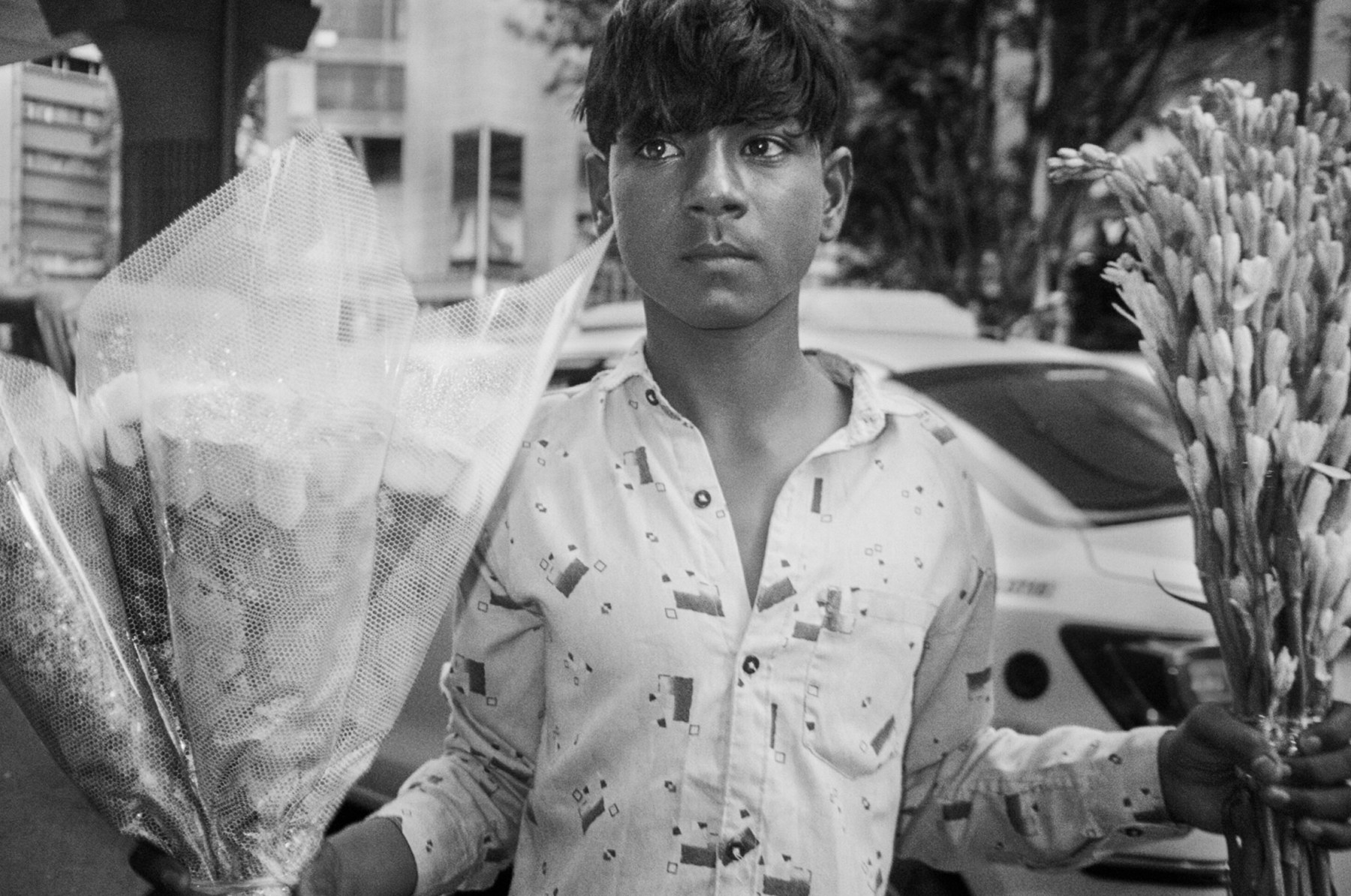 Black and white portrait of a young flower seller holding wrapped bouquets on a city street
