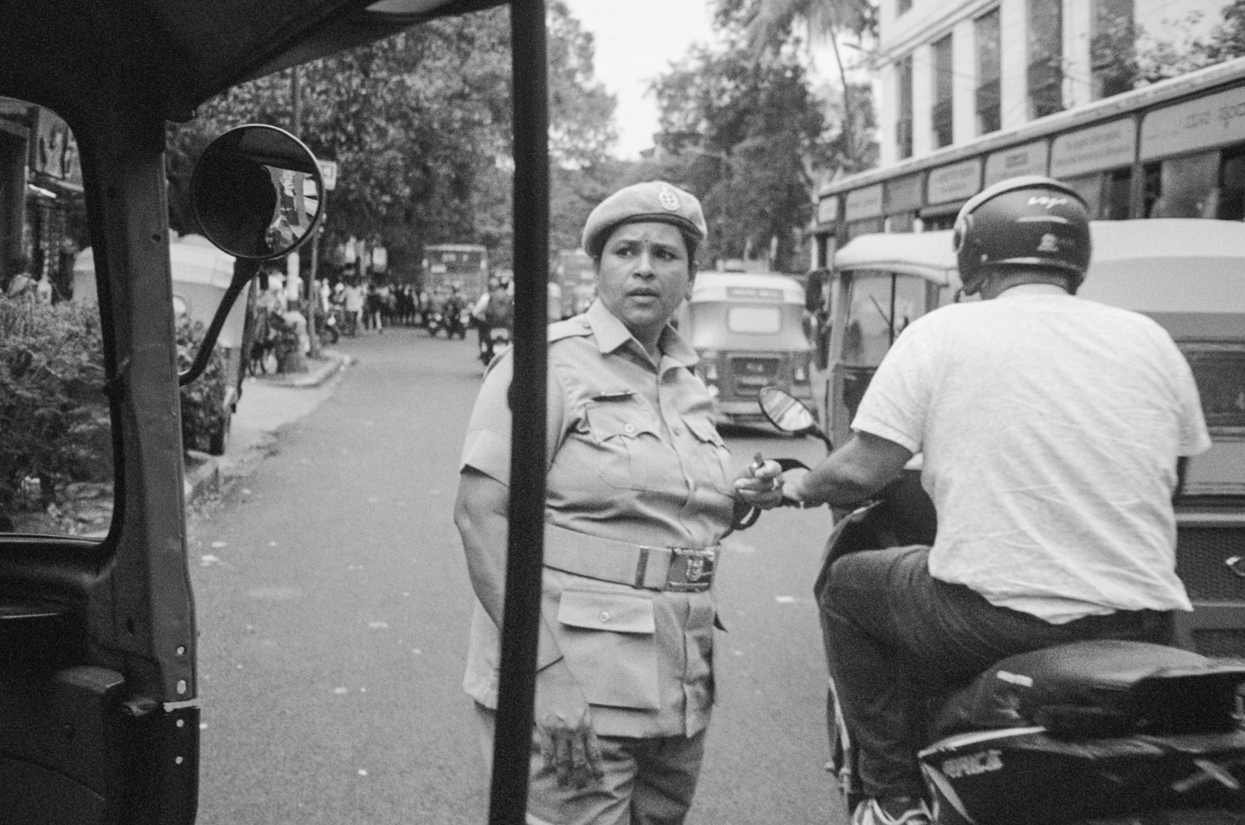 Black and white photograph of a traffic officer speaking to a scooter rider, seen from inside a rickshaw